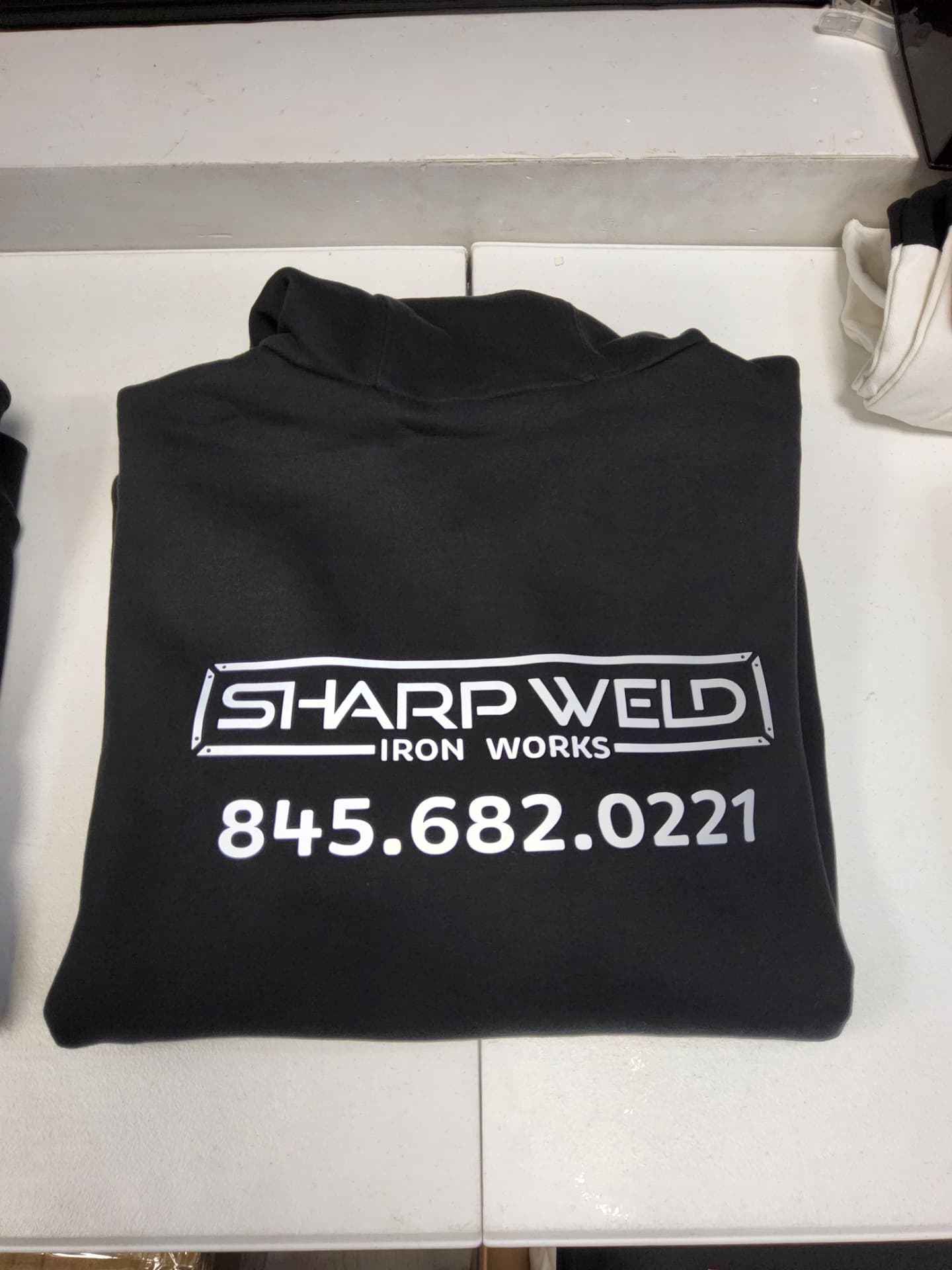 Sharp Weld Iron Works black hoodie with white printed logo and phone number