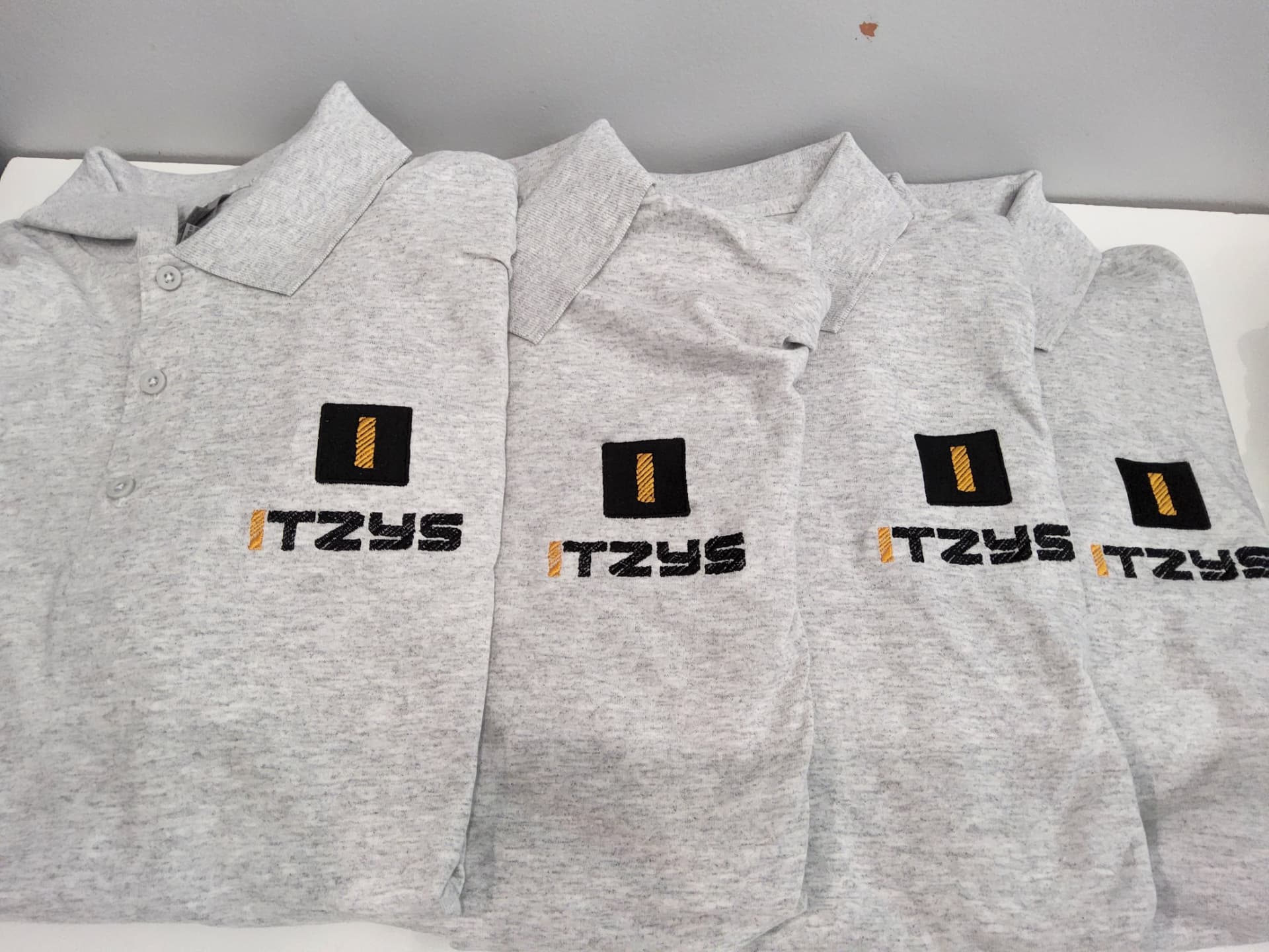 Stack of Itzys grey polos with embroidered black and gold logos